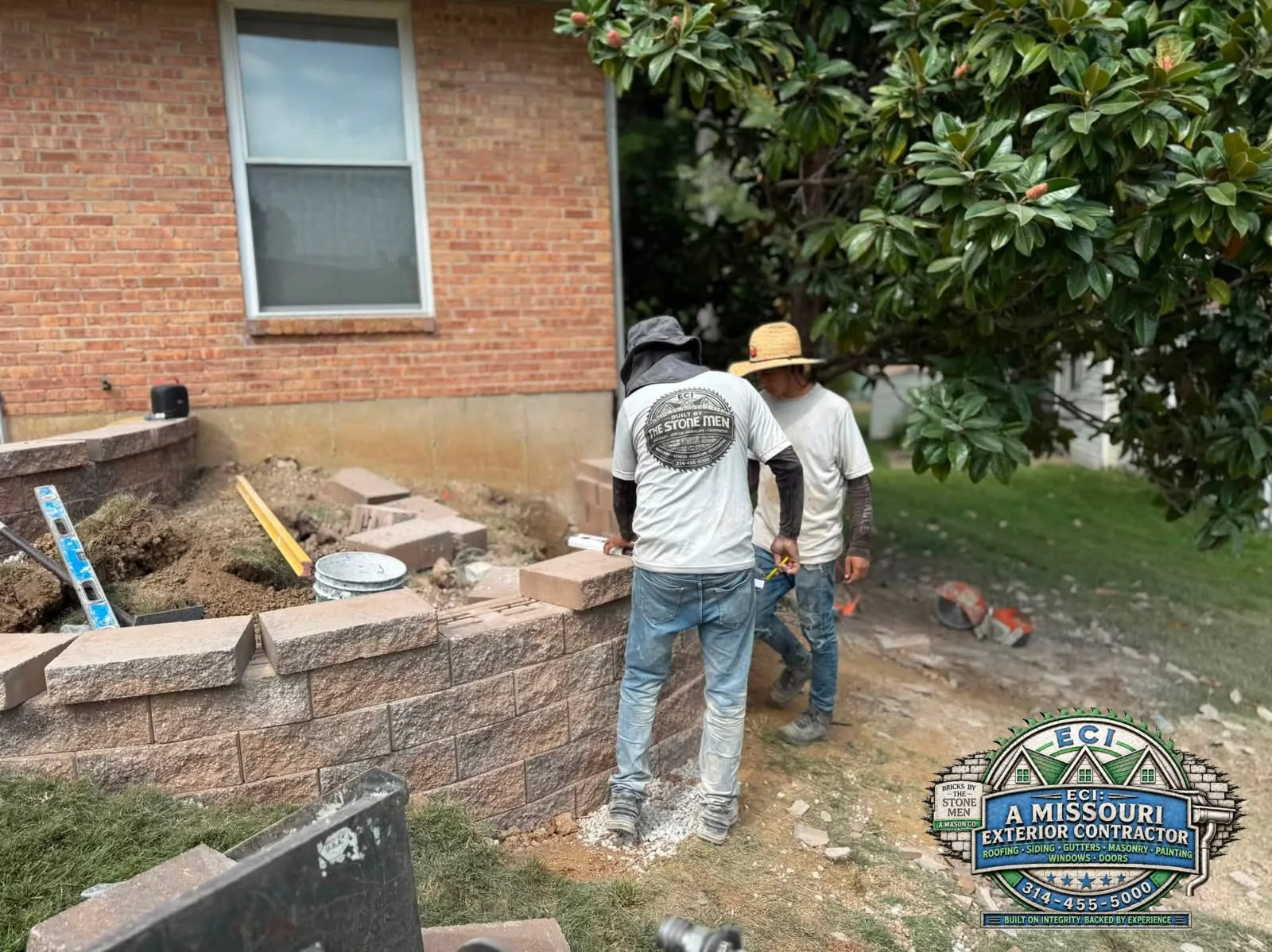 Two crew members working beside a partly built block wall at a residence
