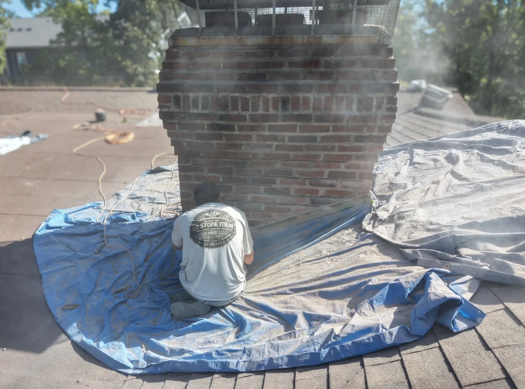 Mason working at the base of a brick chimney on a tarp-covered roof