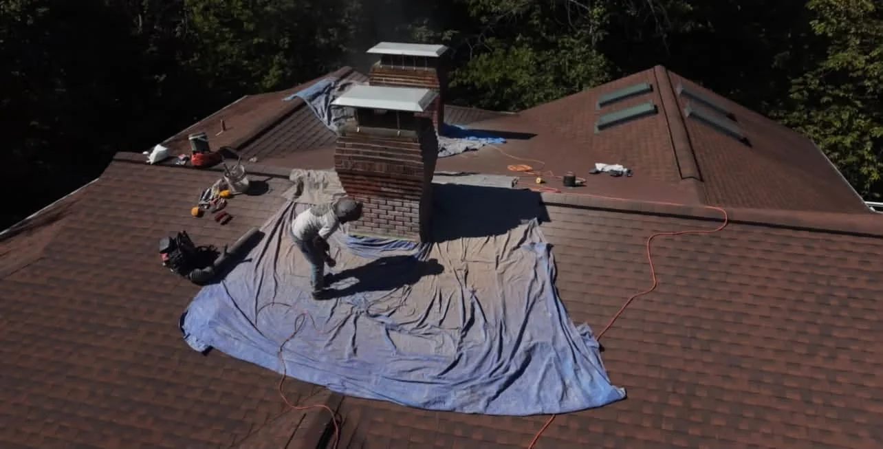 Aerial view of a mason working beside a brick chimney surrounded by roof protection