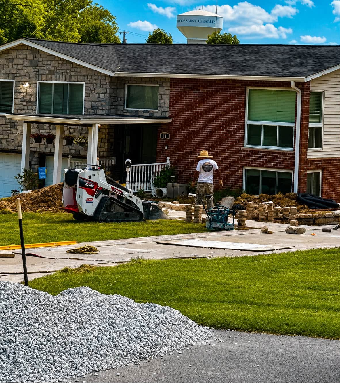 Crew member and compact equipment beside a residential driveway with masonry materials on site
