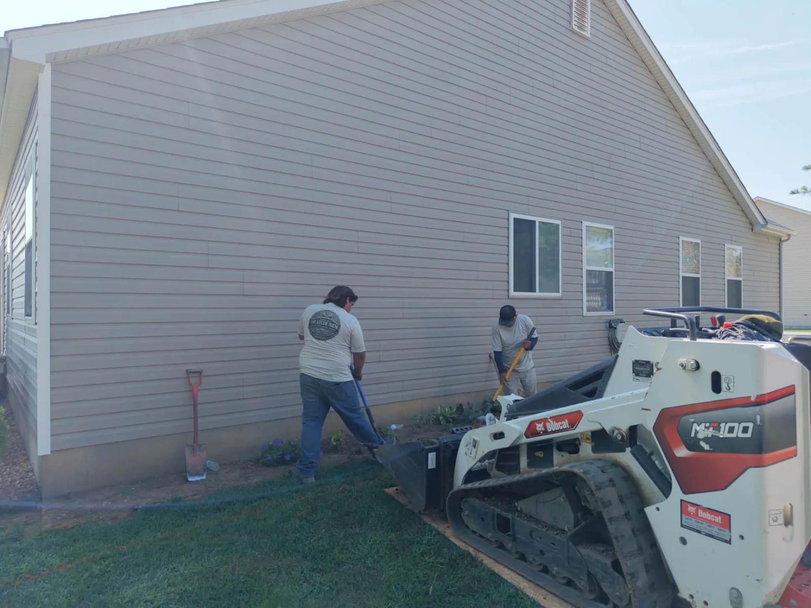 Crew and compact construction equipment beside a house during site preparation