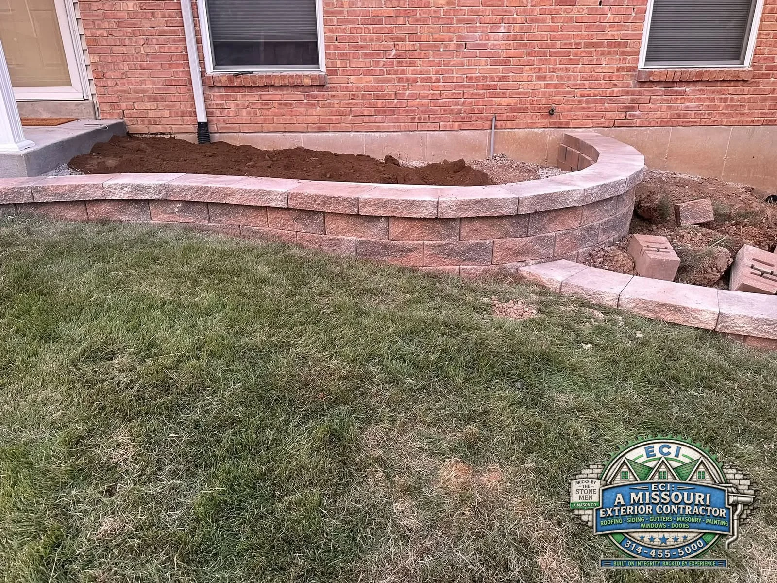 Capped block retaining wall following the grade beside a brick home