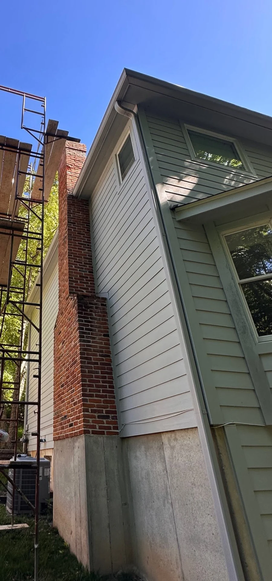 Brick chimney with scaffolding beside a light-sided residence