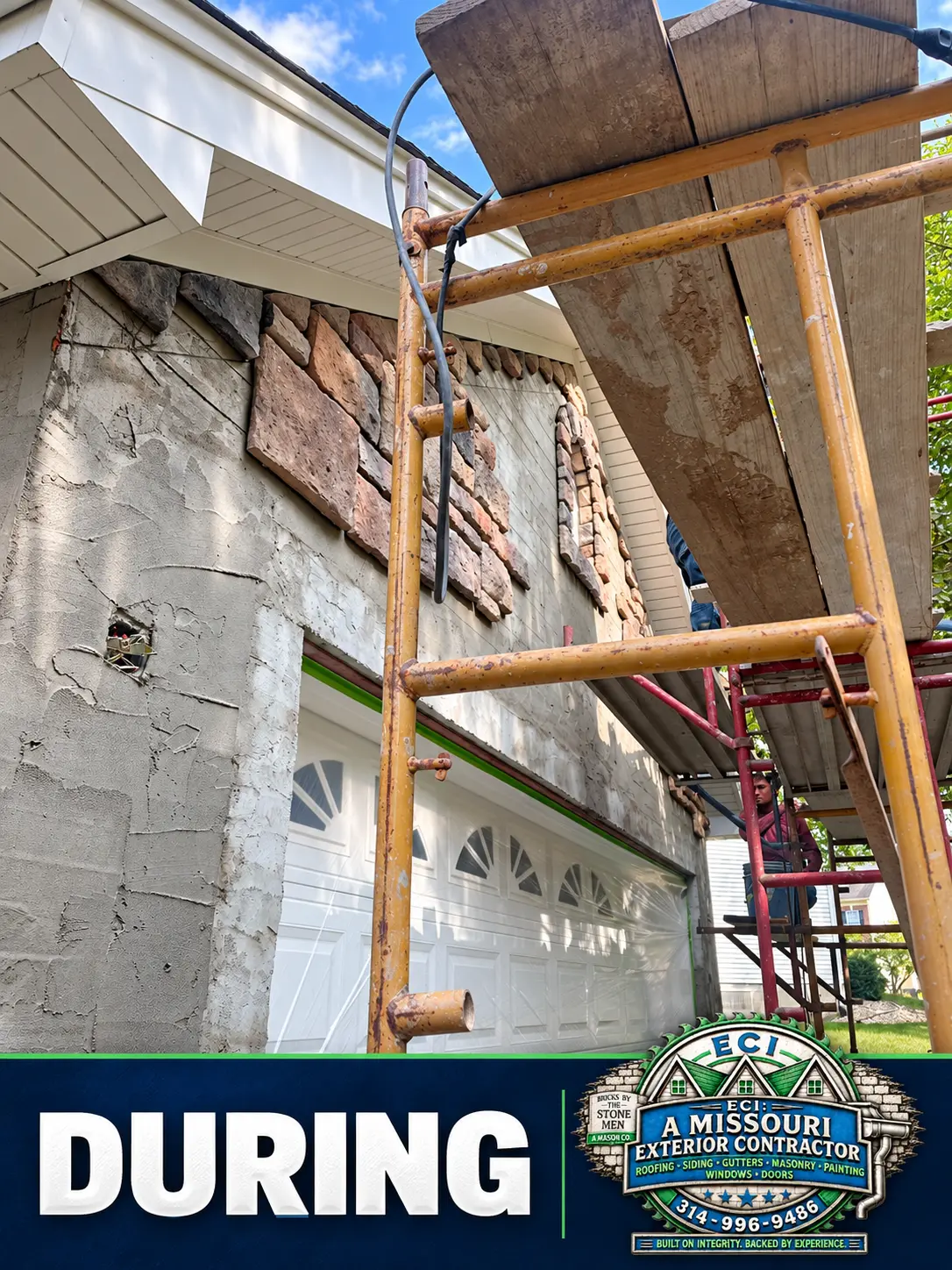 Stone veneer being installed above the garage doors beneath scaffolding